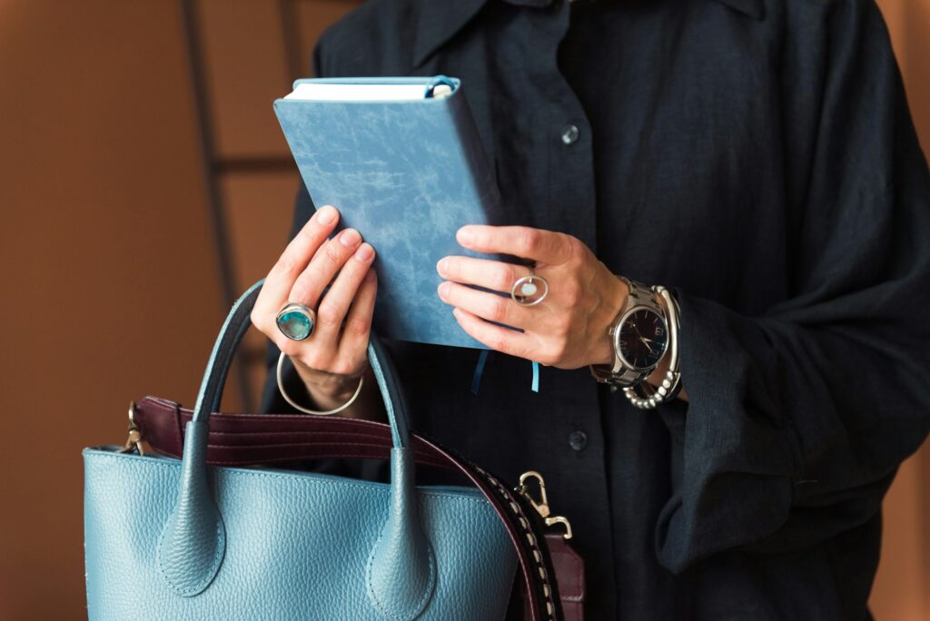 fashionable person holding blue planner and leather bag